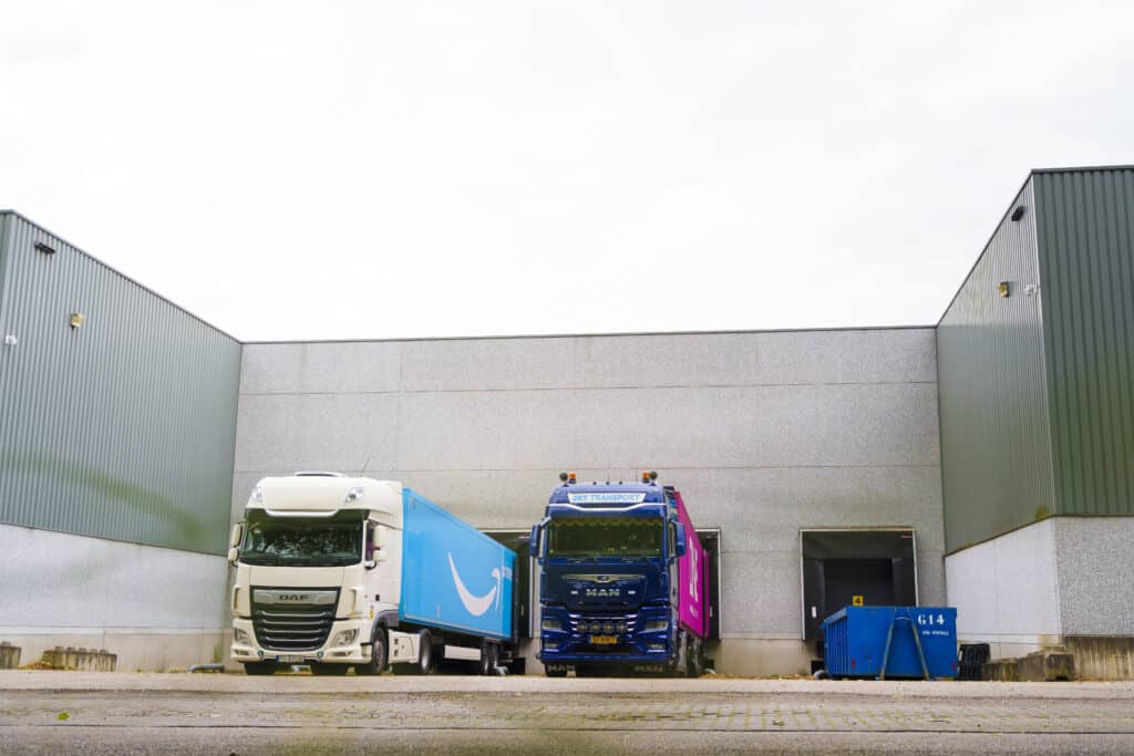 Two transport trucks standing at the loading dock of a warehouse