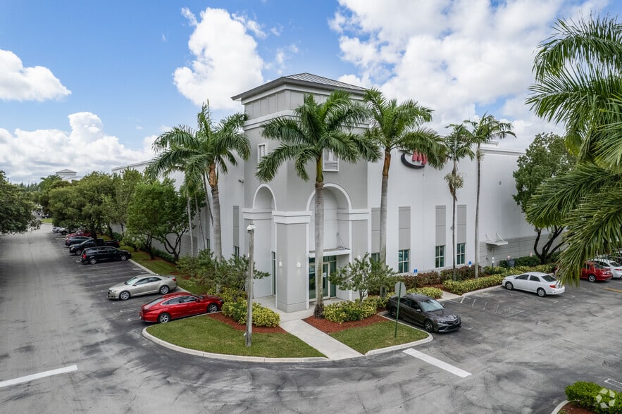 Frontside of grey office buidling surrounded by palm trees