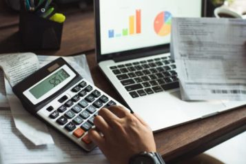 Person sitting at a desk with a laptop, a piece paper and a calculator