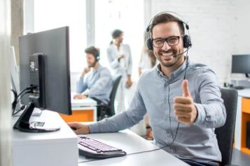 Customer service representative with headset in the office smiling at the camera and giving a thumbs up