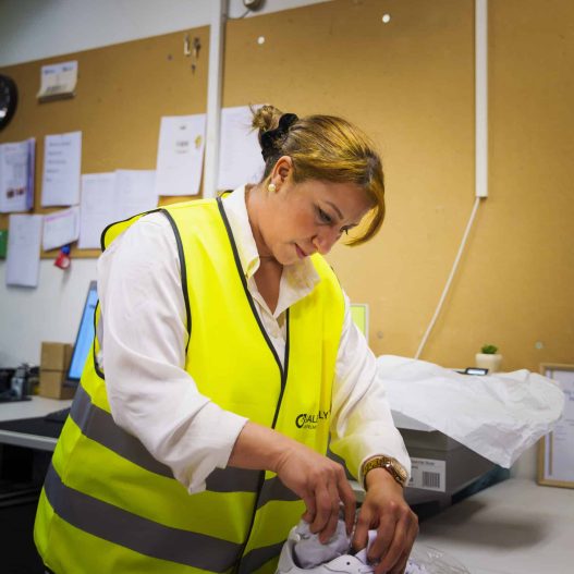 Returns Service Textblock 1 Woman in yellow vest packing a pair of white sneakers in a plastic bag