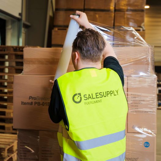 Sales Supply – Warehouse foto’s-60-2 Warehouse worker, seen from the back, wearing a fluorecent Salesupply Fulfillment vest wrapping a pallet of returns