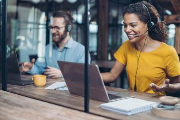 Two customer service representatives with headsets smiling at their computer screens